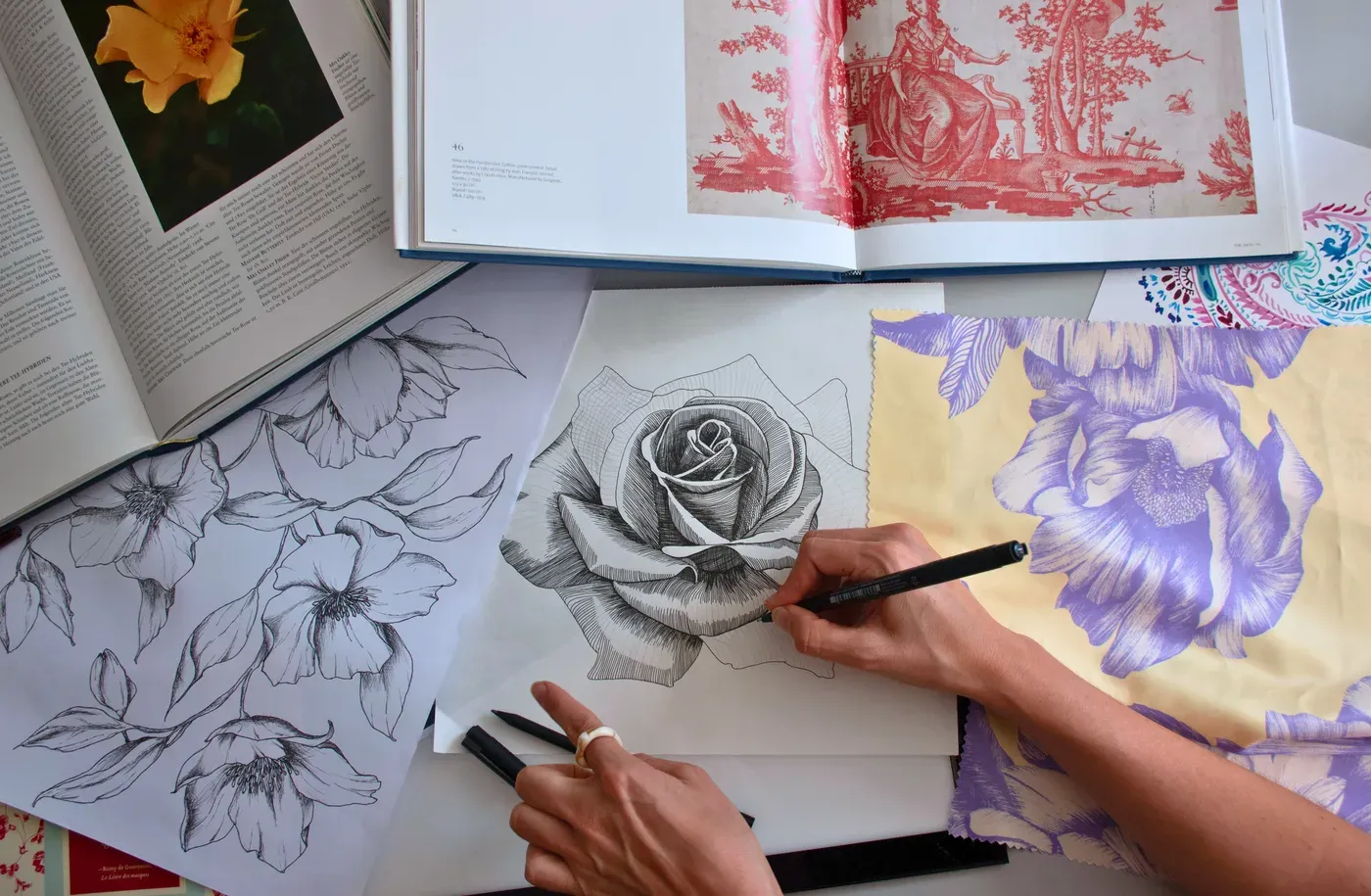 A textile designer drawing a floral print surrounded by fabric samples