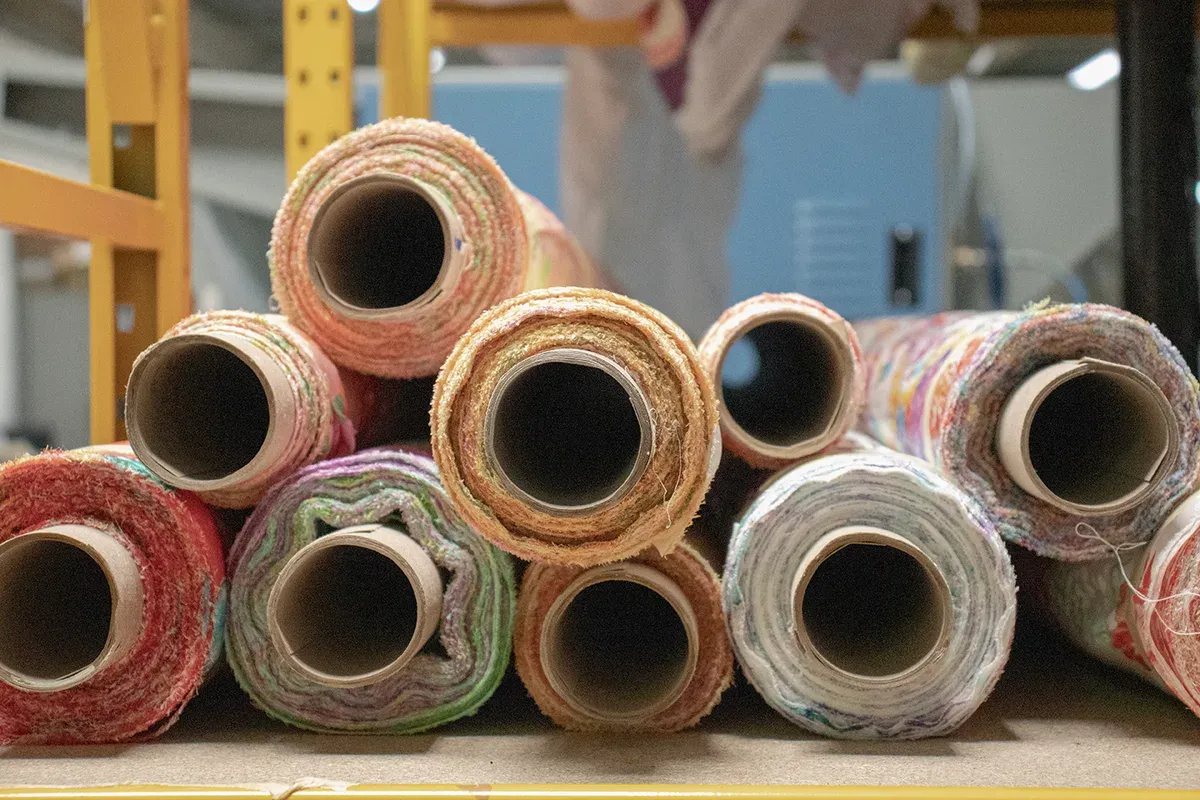 Rolls of recycled textile material stored on a factory rack